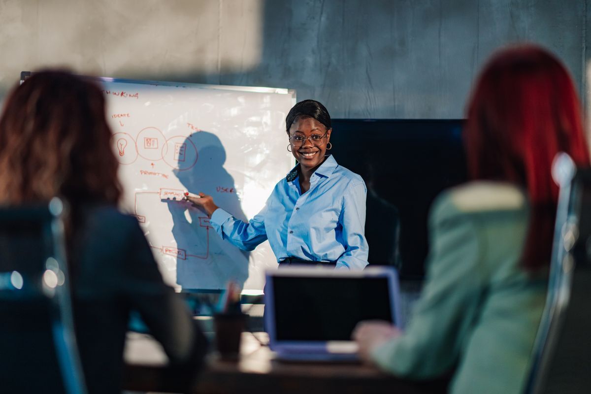 Instructor at a whiteboard explaining a process to two people