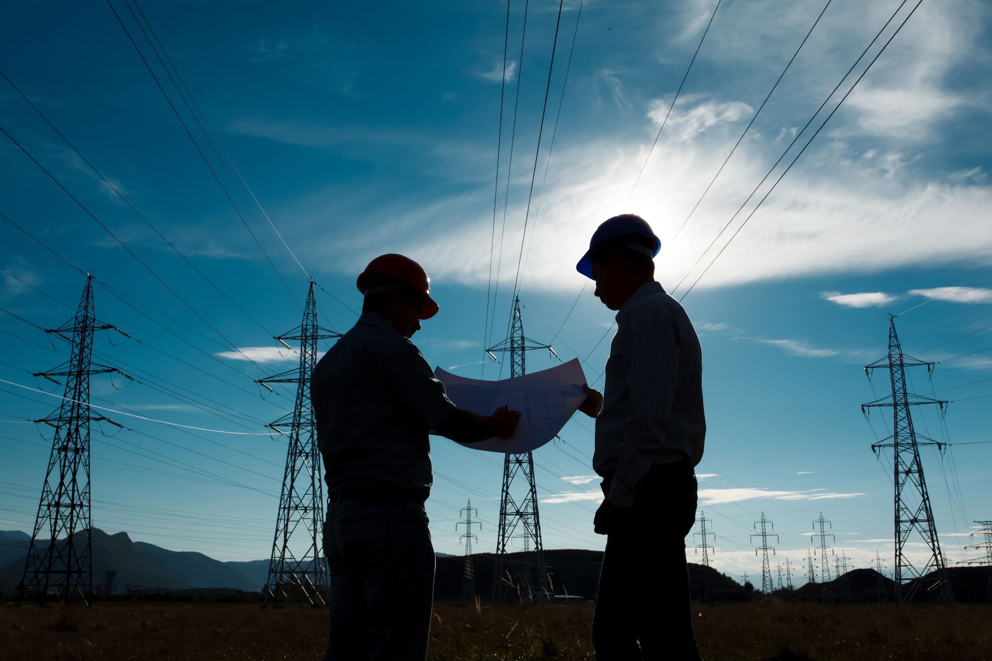 Two engineers reviewing plans beneath transmission lines